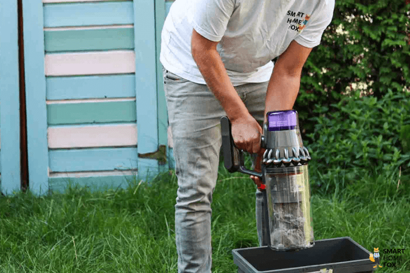 Der Inhalt des Staubbehälters von einem Akkusauger wird in der Mülltonne entsorgt